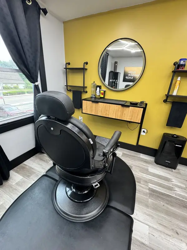Black leather barber chair facing a round mirror and wood vanity